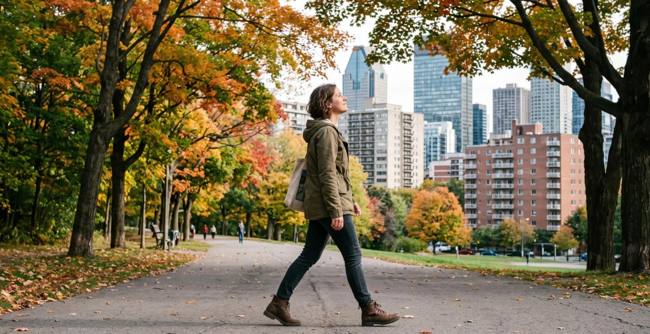 Une personne marche sur un sentier arboré traversant un parc urbain, avec des immeubles visibles au-dessus de la canopée.
